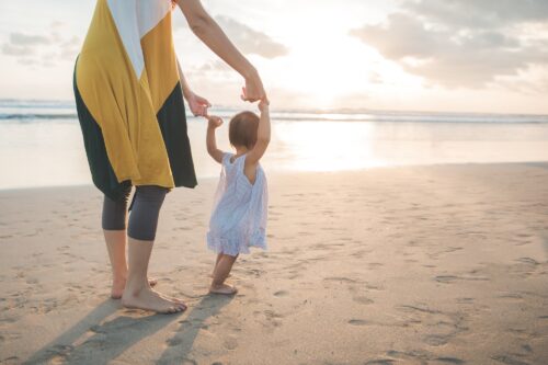 Mother teaching baby to walk on sand
