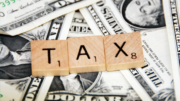 Three Scrabble tiles spelling out the word tax sitting on top of U.S. one dollar bills