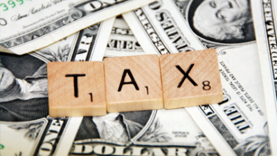 Three Scrabble tiles spelling out the word tax sitting on top of U.S. one dollar bills
