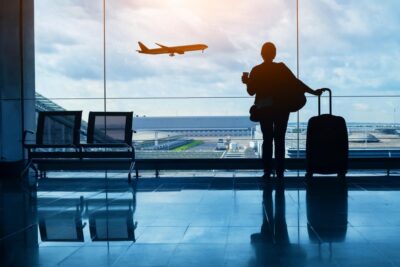 A woman standing with a coffee in her hand, holding luggage, at the airport