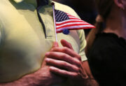 A small American flag being held close to someone's chest wearing a green polo