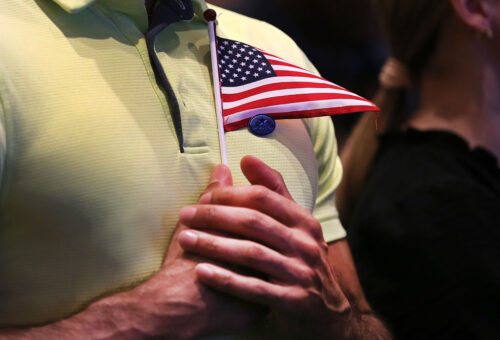 A small American flag being held close to someone's chest wearing a green polo
