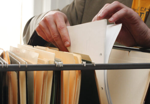 Close-up of a person sorting paper documents in a filing system containing folders and records.