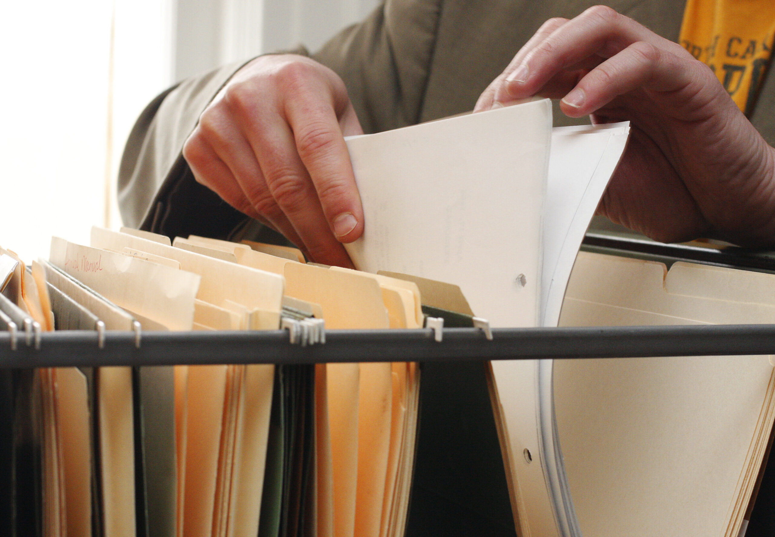 Close-up of a person sorting paper documents in a filing system containing folders and records.