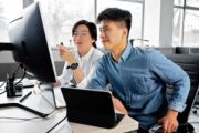 Two professionals reviewing information on a computer in an office environment, representing high-skilled workers who rely on employment-based nonimmigrant visa programs such as H-1B, L-1, and O visas.