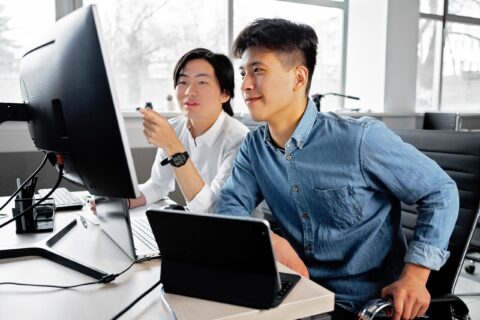 Two professionals reviewing information on a computer in an office environment, representing high-skilled workers who rely on employment-based nonimmigrant visa programs such as H-1B, L-1, and O visas.