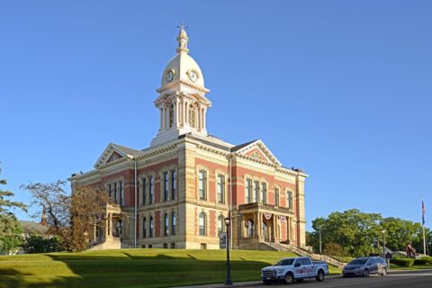 Historic courthouse building in Wabash County, Indiana, featuring a clock tower, red brick and limestone architecture, and a landscaped lawn under a clear blue sky.