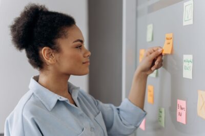 Person placing a sticky note on a planning board covered with colorful notes, representing business strategy, entrepreneurship, innovation, and company growth.