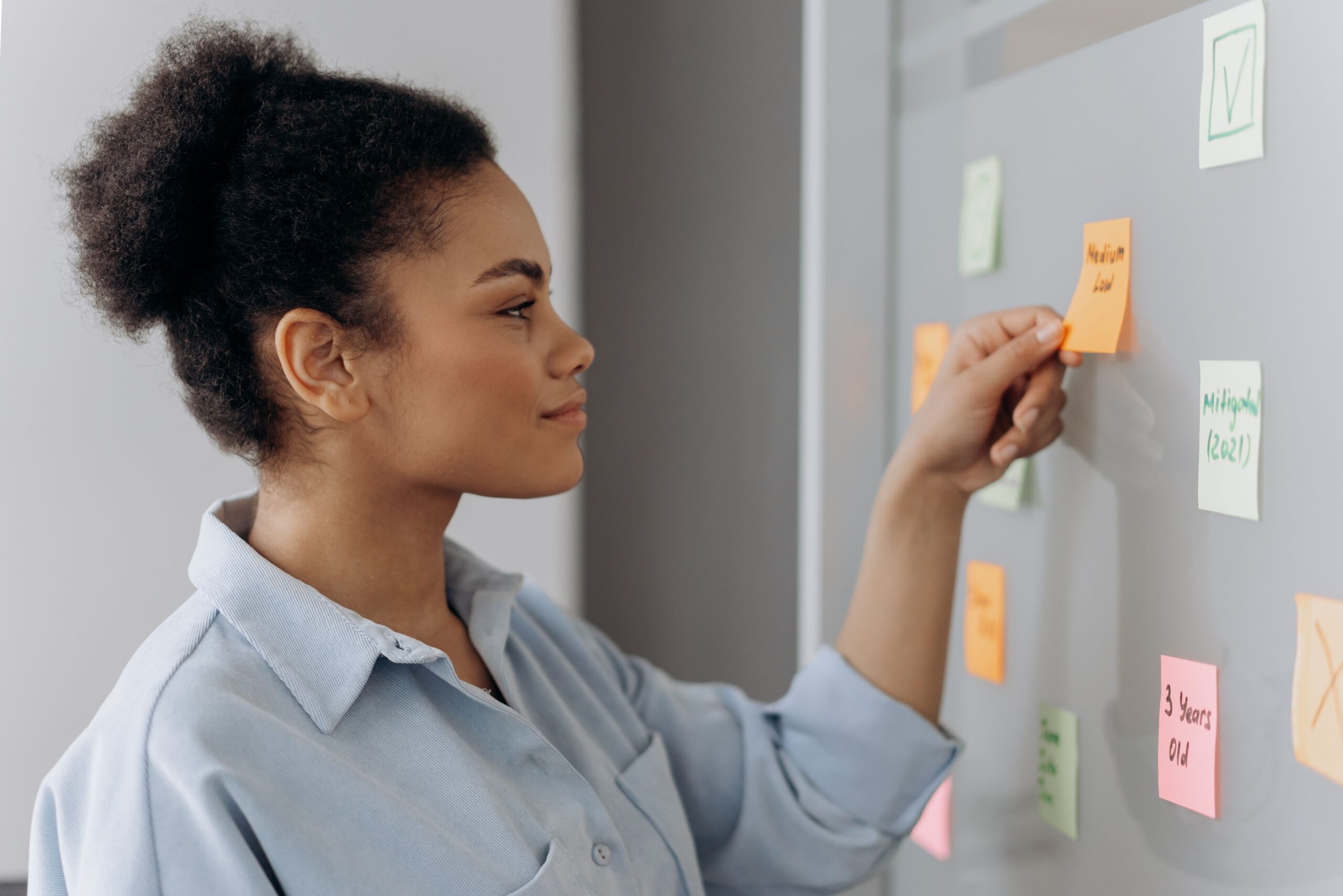 Person placing a sticky note on a planning board covered with colorful notes, representing business strategy, entrepreneurship, innovation, and company growth.